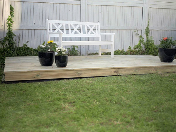 En færdig fritliggende træterrasse med en bænk og blomsterkrukker på