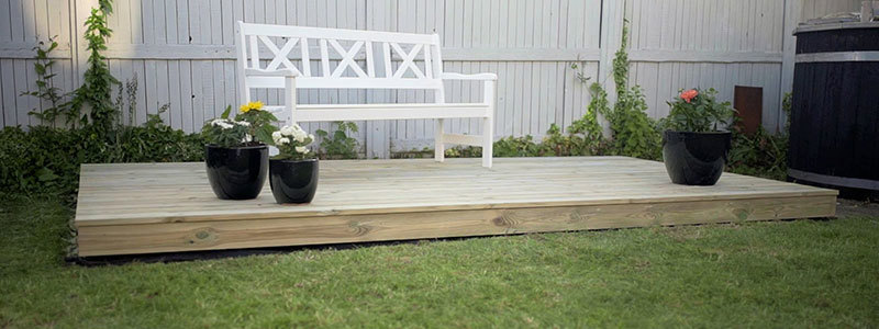 En færdig fritliggende træterrasse med en bænk og blomsterkrukker på