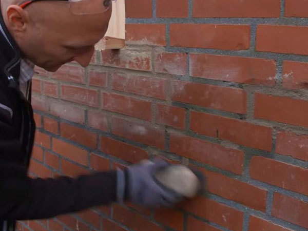 Grater og fugeslør fjernes fra murstenene omkring reparationen